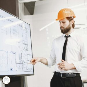Persona con casco de obra señalando un plano técnico en una pantalla, representando la explicación de instalaciones sanitarias y planificación arquitectónica.